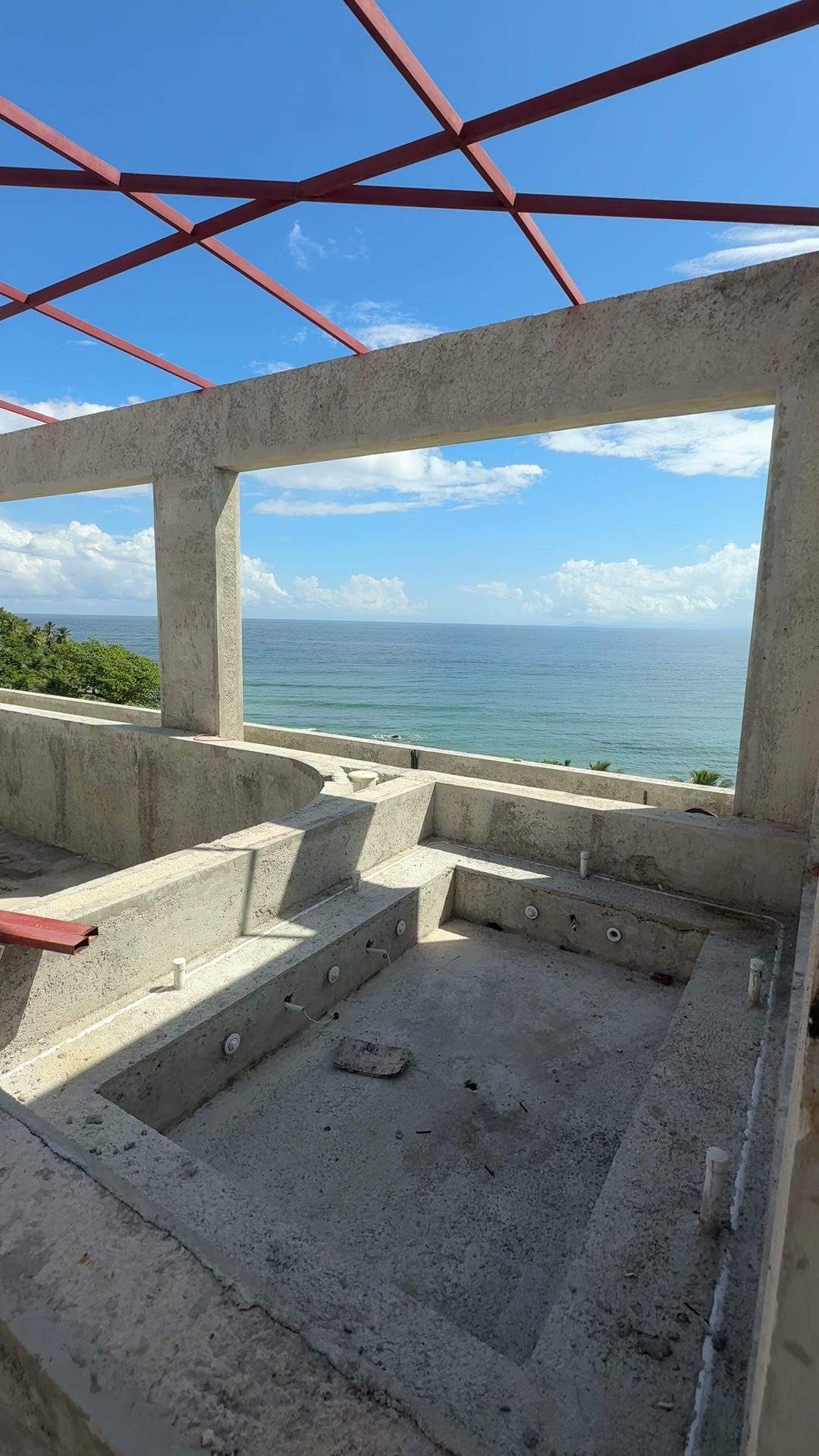 Red steel roof framing over a room open to the sea